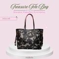 A black and gray floral patterned tote bag with brown leather handles, displayed on a white tiered pedestal against a light pink background with promotional text.
